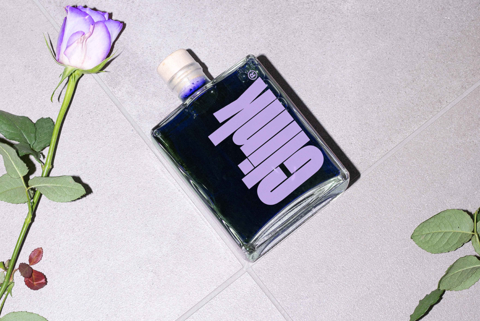 Clear perfume bottle with lavender label next to purple rose buds