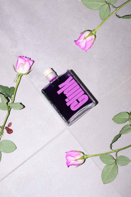 Clear fragrance bottle with hot pink label surrounded by pink roses