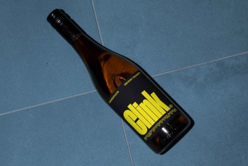 Wine bottle on blue tile background featuring bold yellow text label. Perfect for designers seeking product mockups or wine label graphics.