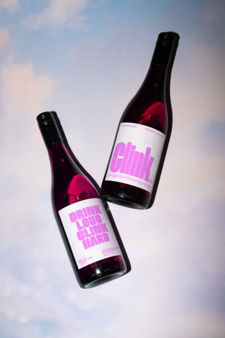 Two wine bottles with bright pink labels against sky background