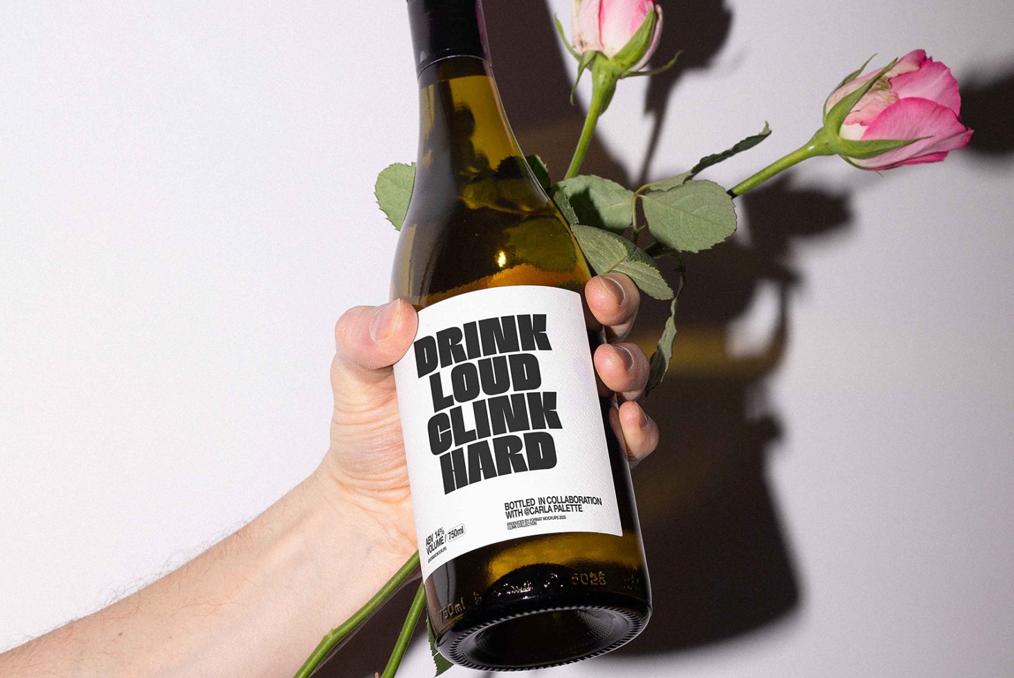 Hand holding a wine bottle with bold typography on label Drink Loud Clink Hard paired with pink roses ideal for graphic design mockups branding projects