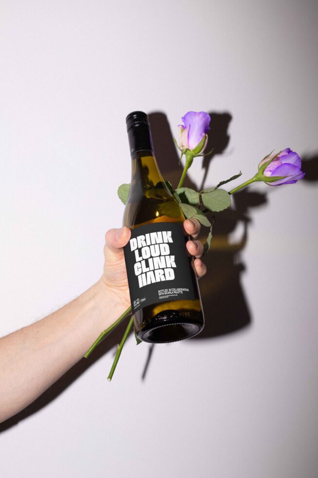Hand holds wine bottle with bold label lettering and purple roses. Perfect for graphic design mockups templates. Creative product branding photography.