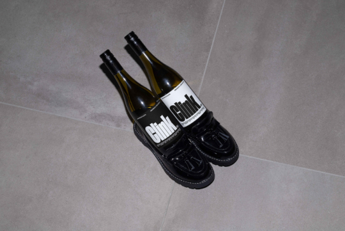 Two wine bottles labeled Clink in black patent shoes on stone tile floor. Perfect for graphic design inspiration and mockup projects.