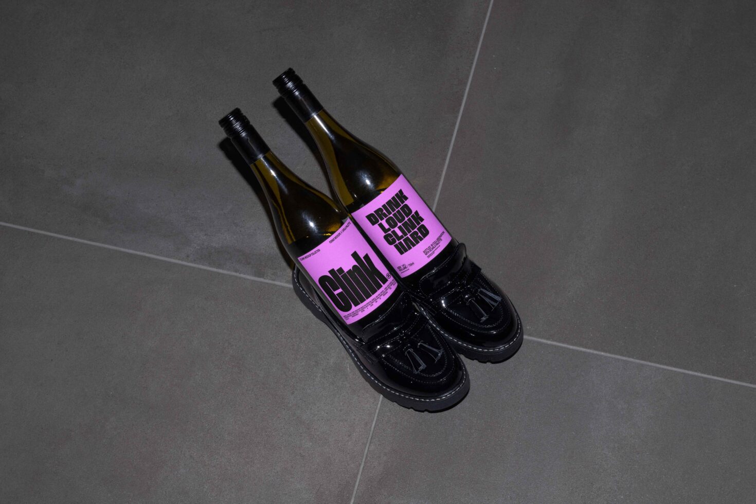 Two wine bottles with purple labels placed in black shoes on a gray tile floor. Ideal for graphic designers seeking unique mockup inspiration.