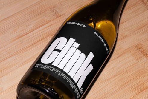 Wine bottle mockup featuring bold typography on a black label with a modern design on a wooden surface. Ideal for branding and packaging designs.