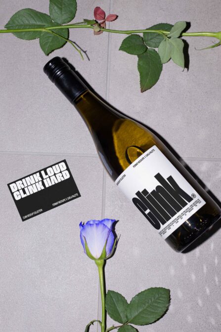 Wine bottle with black label next to business card, fresh roses scattered on tiles
