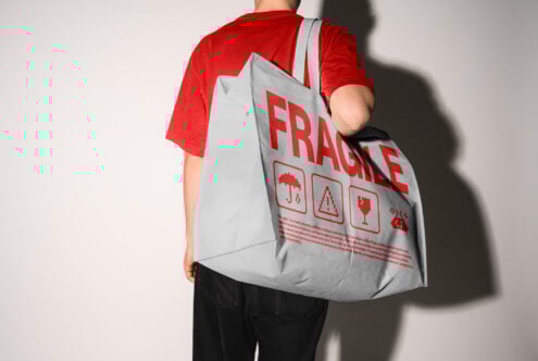 Mockup of a person carrying a large gray tote bag with red Fragile text and icons, ideal for packaging design and marketing concepts in graphic design.