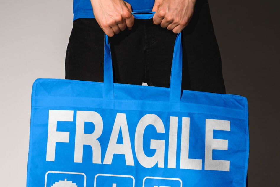 Bright blue tote with white fragile lettering, held by hands showing strong grip