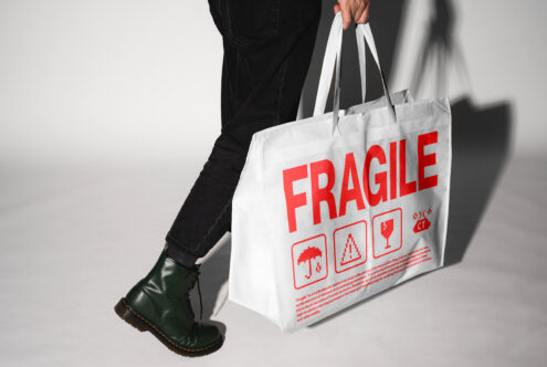 Person carrying large white bag with red Fragile text mockup design template. Keywords: mockup, design, template, bag, Fragile, packaging, minimalist.