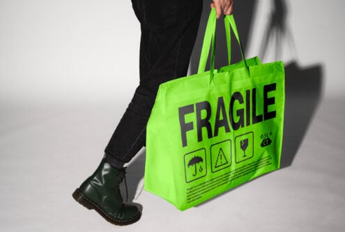 Designer holding bright green tote bag with Fragile text in bold black font. Creative mockup for eco-friendly product packaging or graphic design assets.