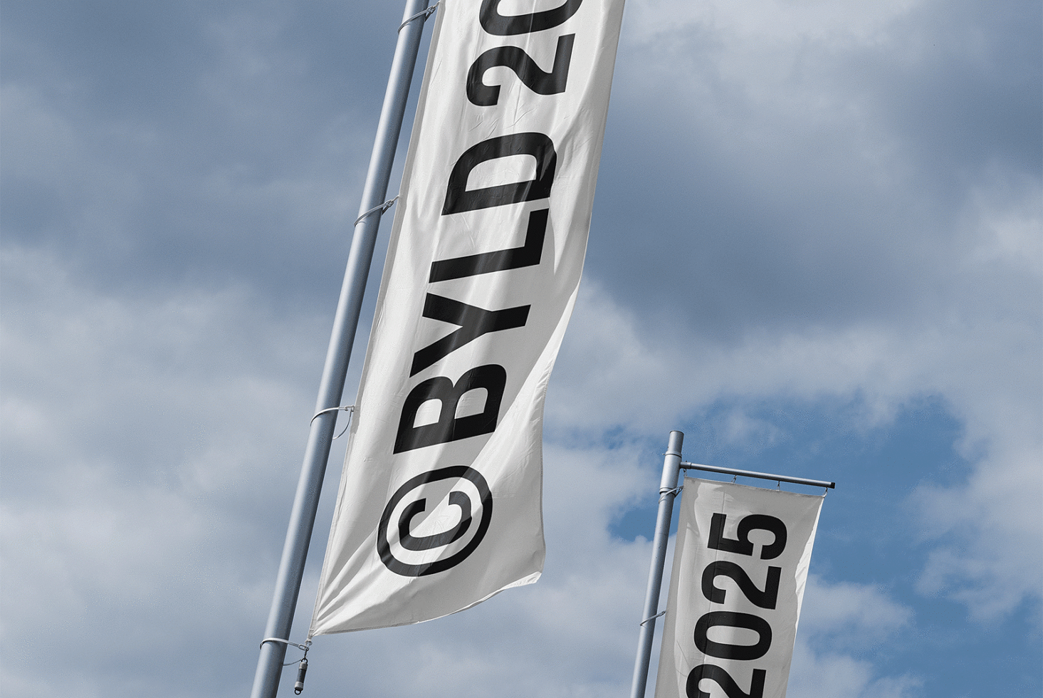Two vertical flags on poles against a cloudy sky labeled with BYLD 2025. Perfect for graphic and mockup designers needing sky-themed templates and concepts.