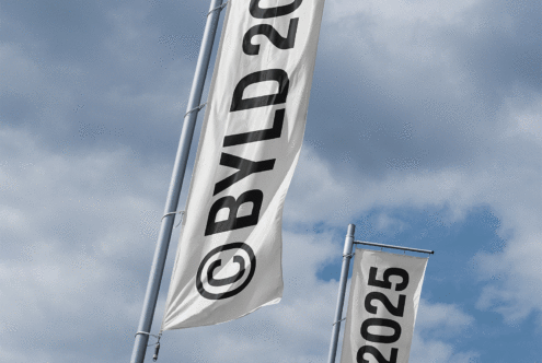 Two vertical flags on poles against a cloudy sky labeled with BYLD 2025. Perfect for graphic and mockup designers needing sky-themed templates and concepts.
