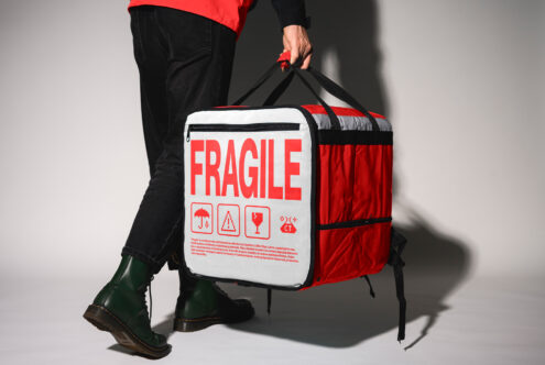 Person holding a red and white insulated delivery backpack with Fragile text; ideal for mockups, branding, ecommerce, shipping, package design projects.