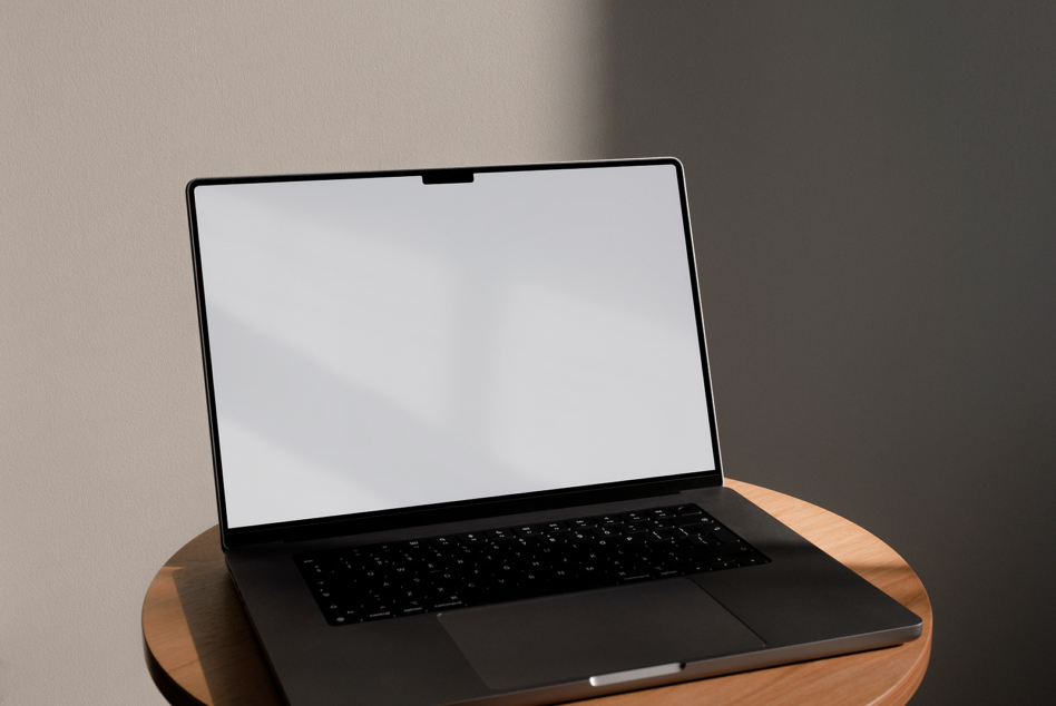 Laptop on circular wooden desk with blank white screen showing window light