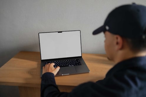 Man using a laptop with a blank screen on a wooden desk suitable for mockup designers keyword mockups templates digital assets design tools