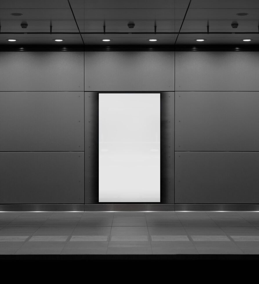 Subway billboard mockup with blank white poster surrounded by metallic wall panels and overhead lighting. Ideal for showcasing ad designs and graphics.