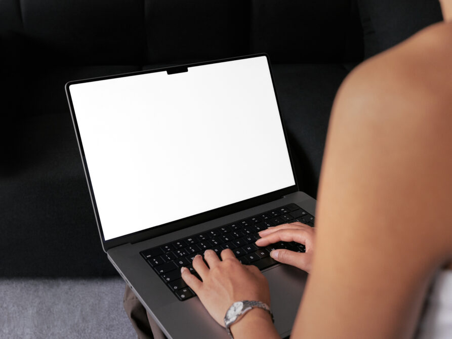 Overhead view of hands typing on laptop with blank white screen display