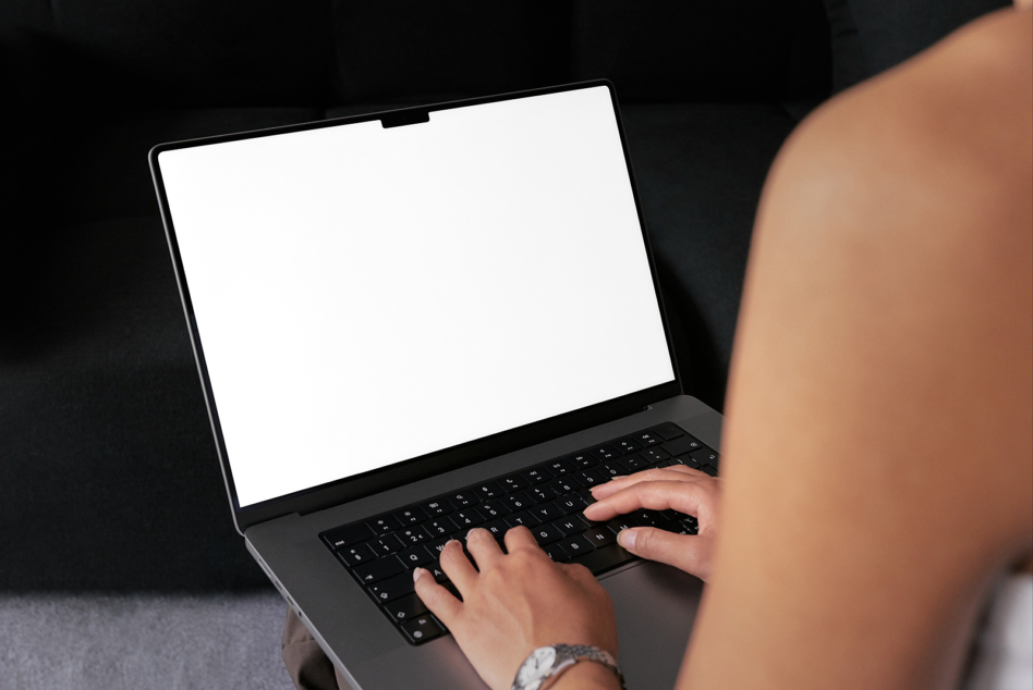 Person typing on laptop with blank white screen, wearing watch