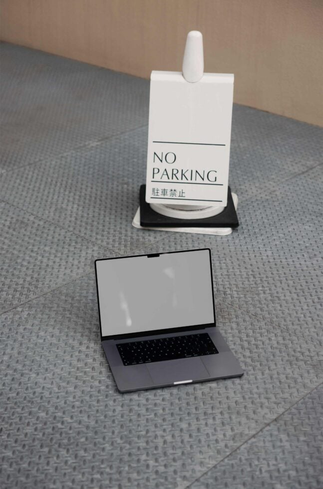 Laptop mockup on textured floor beside no parking sign. Ideal for showcasing tech designs or graphic projects. Perfect for designers seeking realistic scenes.