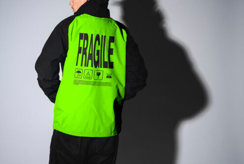 Man wearing neon jacket with Fragile text and icons, standing against gray background. Fashion mockup suitable for designers, graphics, templates.