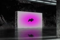 Large screen displaying hot pink gradient logo in raw concrete warehouse space