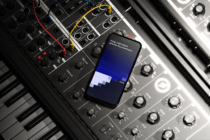 iPhone 14 Pro angled on music gear setup with colorful cables, blue gradient display
