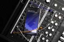 iPhone 14 Pro on synth mixer with orange cable, blue gradient screen showing app interface