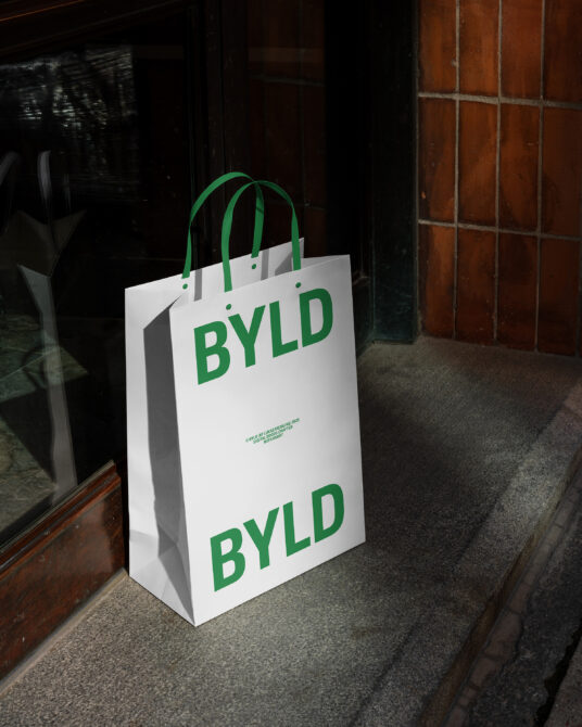 White bag with green BYLD text stacked, green handles in dark alley