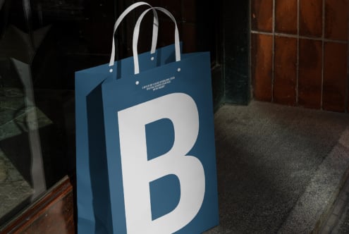 Blue paper bag mockup with large white B design standing against brown tiled wall. Ideal for branding, packaging, marketing, and graphic design projects.