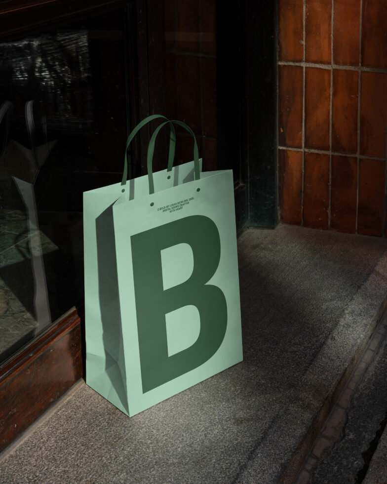 Green shopping bag mockup featuring large letter B, placed against urban wall. Ideal for branding, packaging design, retail marketing, product display.