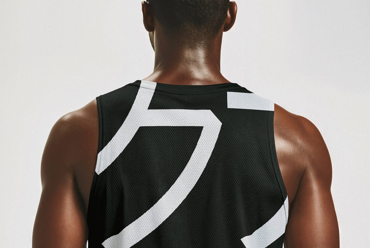 Back view of a person wearing a black mesh sports jersey with bold white graphic elements. Ideal for athletic apparel mockups or graphic design templates.