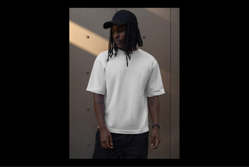 Tshirt mockup featuring a man in a blank white tee and black cap standing against a modern background. Ideal for apparel design presentations.