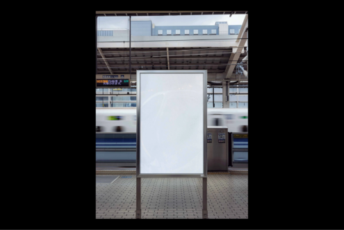 White vertical billboard in a train station platform with a blurred moving train behind. Ideal for mockup design in urban advertising and marketing projects.