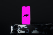 Device display showing solid magenta with brand logo on marble textured phone stand