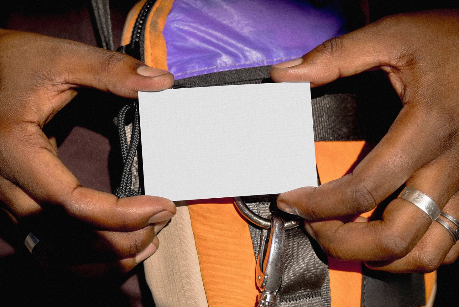 Person holds blank business card mockup in front of colorful backpack. Perfect for designers seeking customizable stationery templates for branding.
