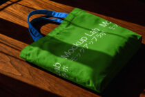 Bright green tote bag with blue handles on warm wood backdrop