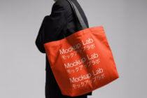 Bright red tote bag with Mockup Lab text repeated, gray shoulder strap visible