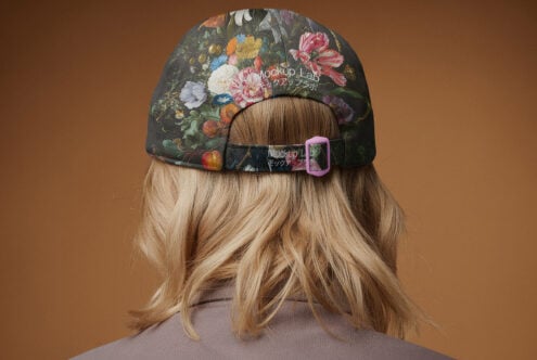 Floral cap design mockup featuring a person with long blonde hair wearing a fabric cap with colorful flower patterns and adjustable strap. Fashion template.