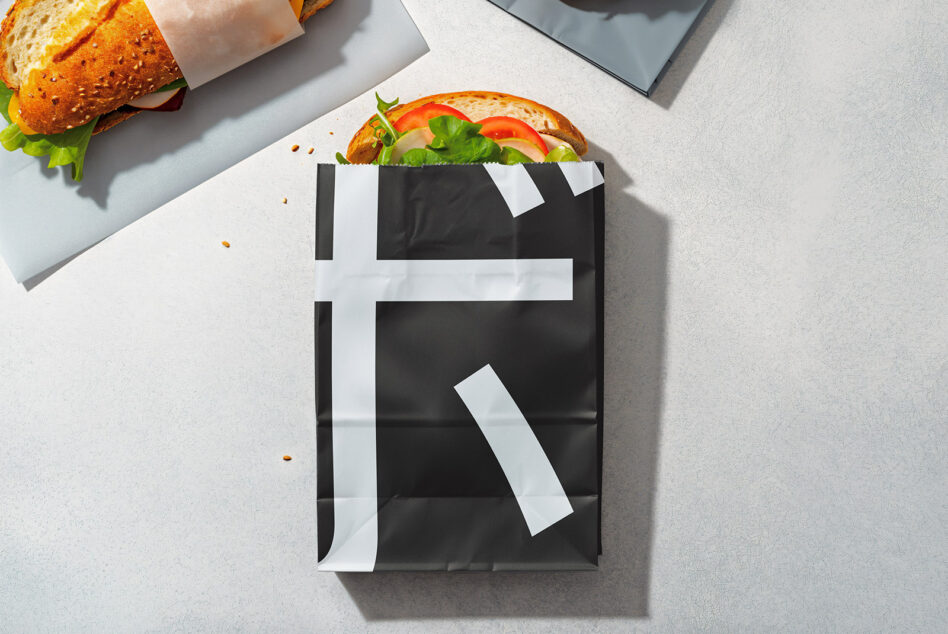 Black paper food packaging with white tape holding toasted sandwich above