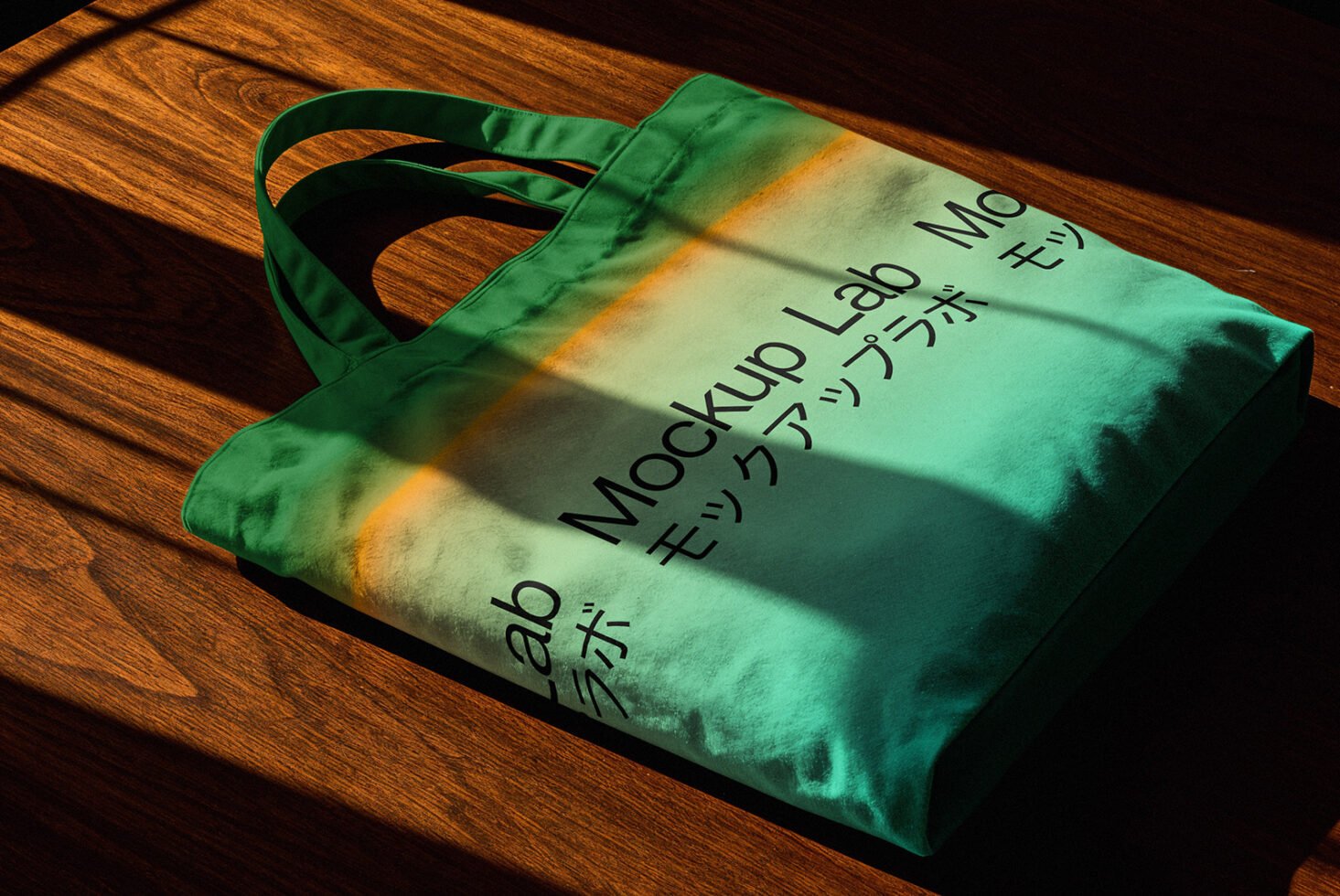 Green tote bag mockup with shadow overlay on wooden surface featuring Japanese text. Ideal for showcasing branding designs. Perfect for graphic designers.