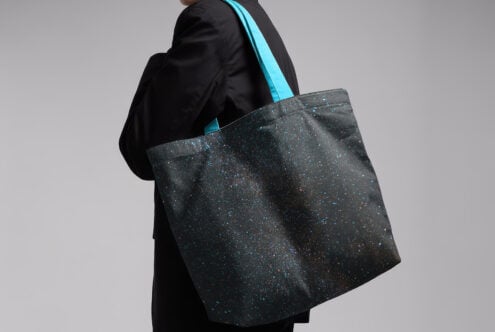 Designer mockup featuring tote bag with galaxy print and turquoise handles worn by a person in black jacket ideal for fashion graphics templates