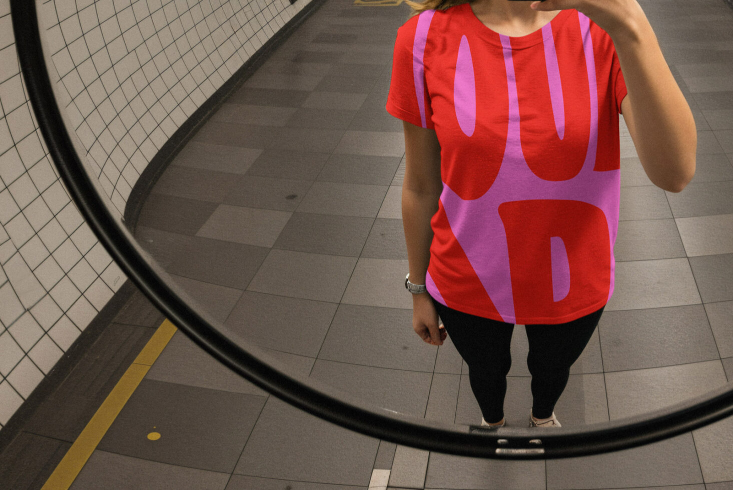 Person in a subway mirror wearing a bold red and purple graphic tee shirt template. Ideal for designers seeking unique apparel mockups or digital assets.