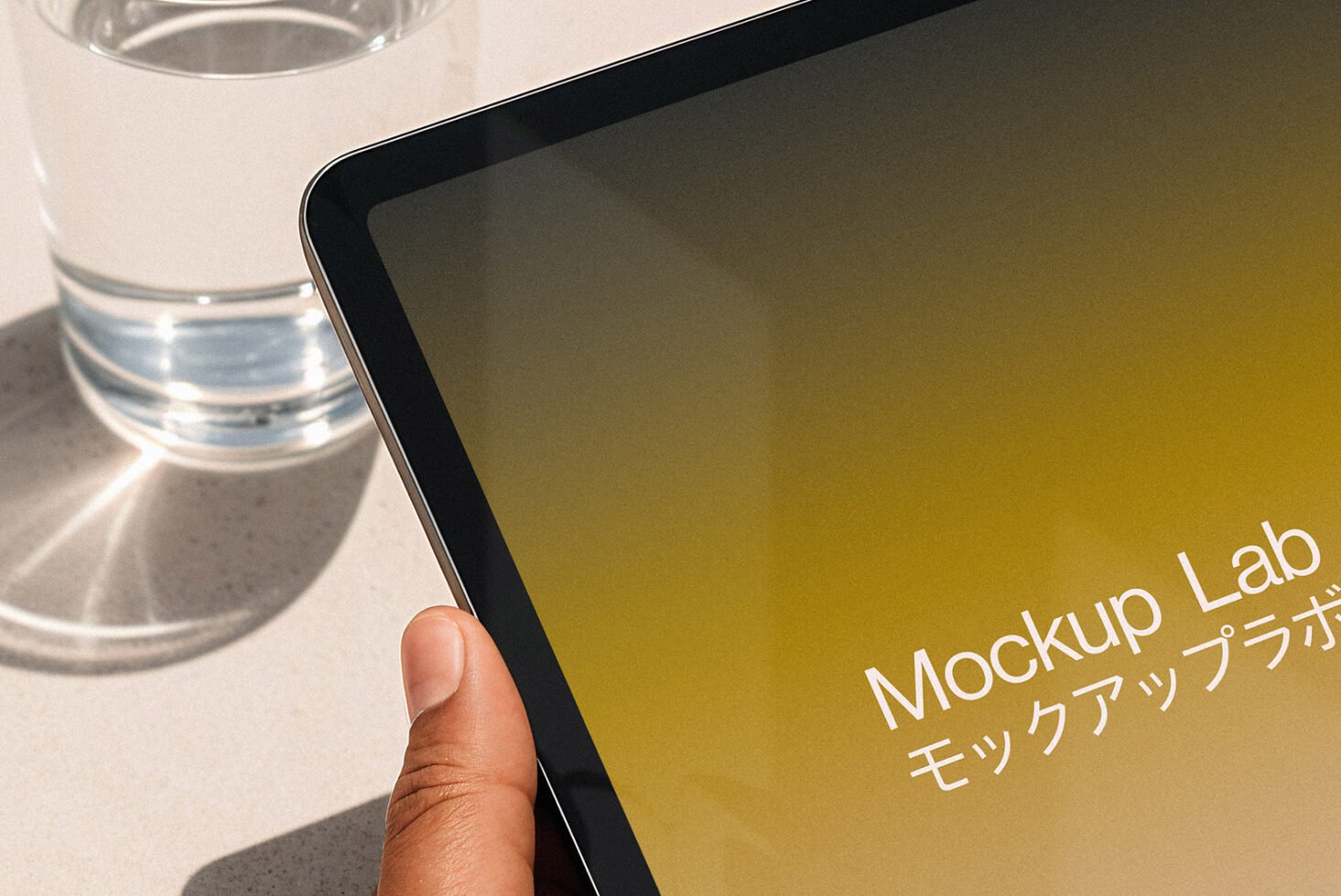 Tablet mockup held by hand next to a glass of water on a table. Yellow gradient screen with text. Ideal for digital designers. Mockups category.