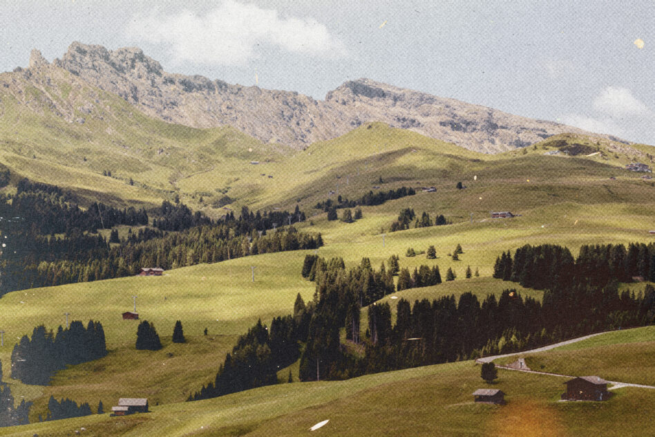 Rolling alpine meadow with scattered cottages, forested slopes, distant mountains