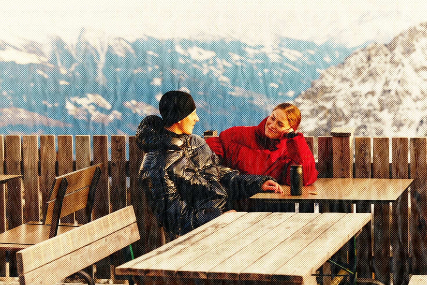 Two people in winter clothing sit at an outdoor cafe with snowy mountain views in the background. Perfect for mockup designs or adventure templates.