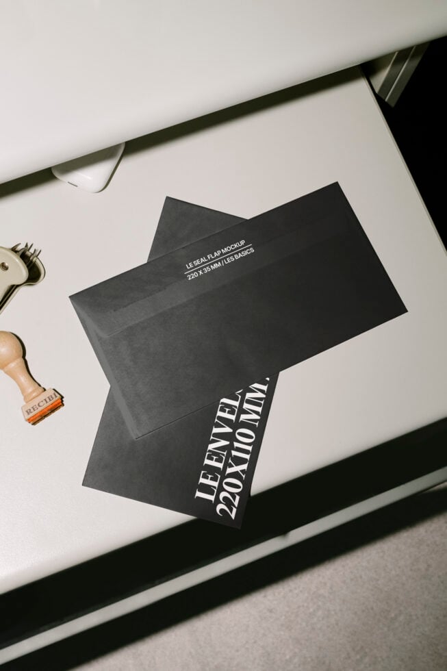Black envelope mockup on a white desk with a stamp. Perfect for designers seeking modern stationery templates. Keywords: mockup, envelope, stationery.