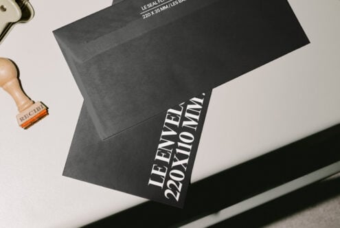 Black envelope mockup featuring measurement text, ideal for designers. Includes wooden stamp tool. Perfect for branding and stationery design presentations.