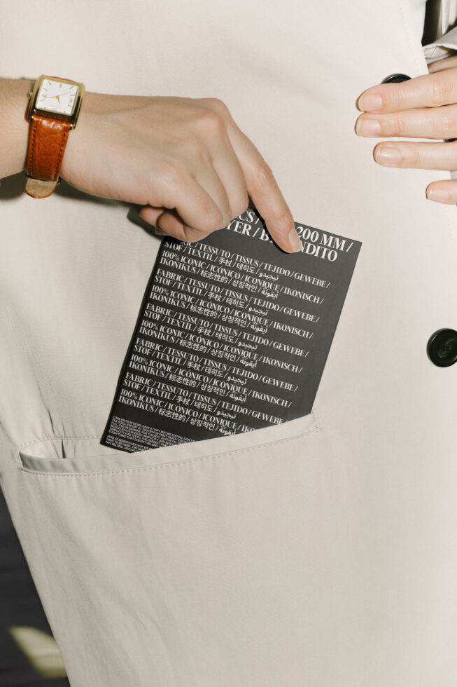 Hand placing black card with text into beige coat pocket, wearing brown leather watch. Ideal for mockups, fashion template, graphic design use.
