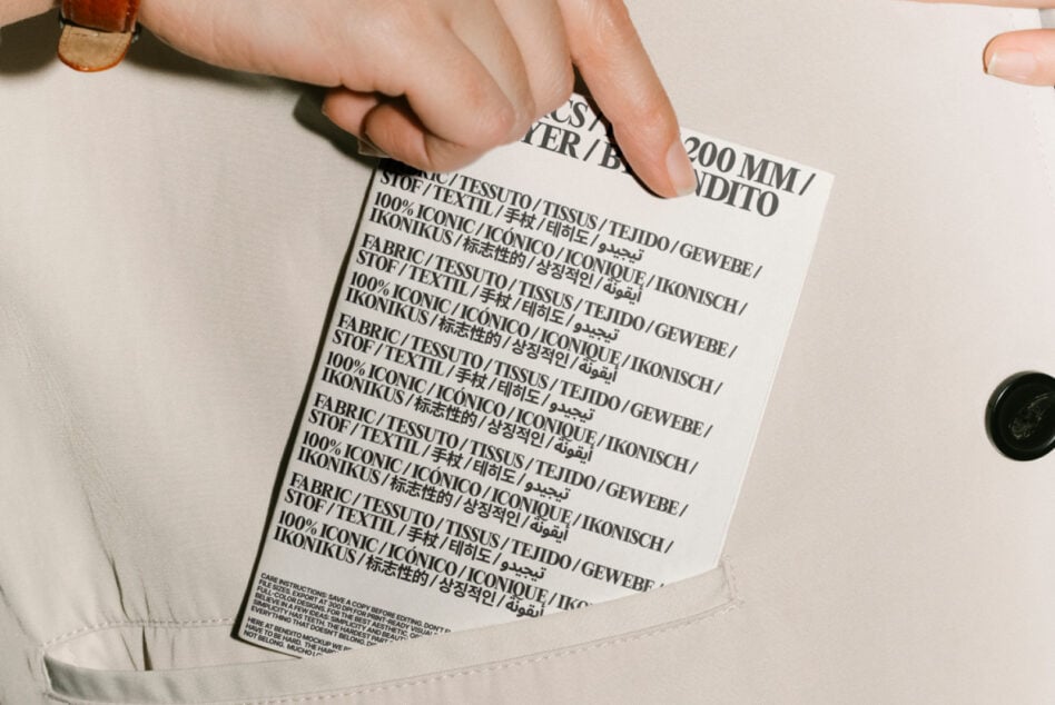 A hand holding a fabric label with multilingual text on a beige garment. Ideal for textile designers needing realistic mockups and creative templates.
