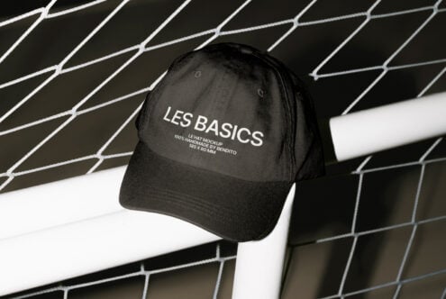 Black cap mockup with white text leaning on a wire fence design perfect for graphic templates fashion prototypes design assets mockups for designers